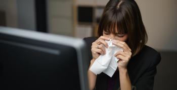 A woman working at home blowing her nose into a tissue.
