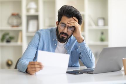 Man looking frustrated while he looks at a piece of paper. 
