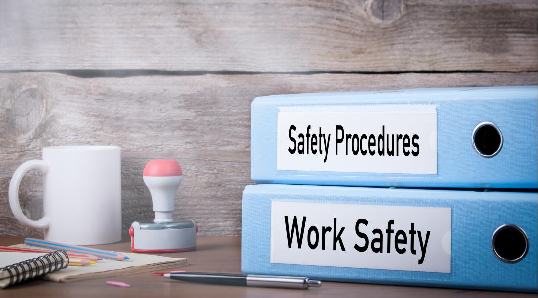 Work safety and Safety procedure binders on a desk with a coffee mug and other desk items.